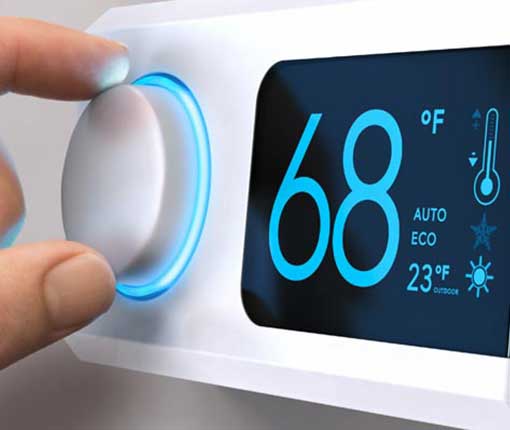Image of electronic thermostat with human fingers on the dial